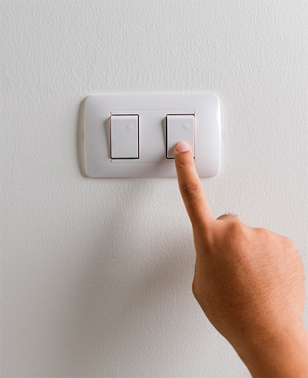 A person's hand turning off a light switch.