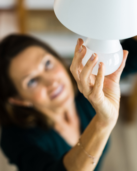 A woman installs a lightbulb into a celling fixture.