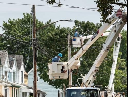 Utility workers in bucket trucks work on overhead cables.