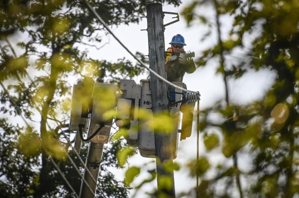 A Con Edison worker is working in raised bucket, repairing overhead power lines. 