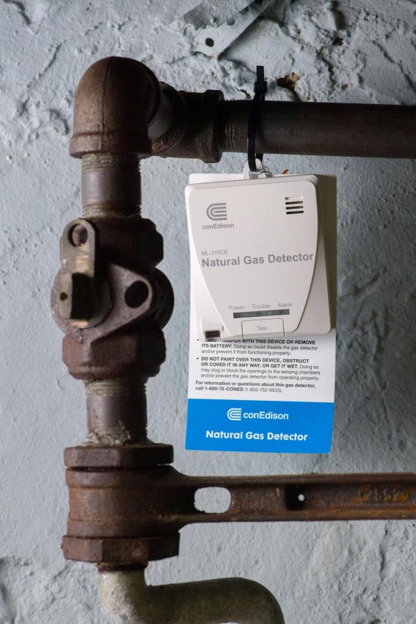 A gas detector hangs from a pipe.