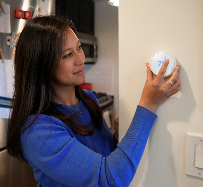 A woman adjusting a thermostat.
