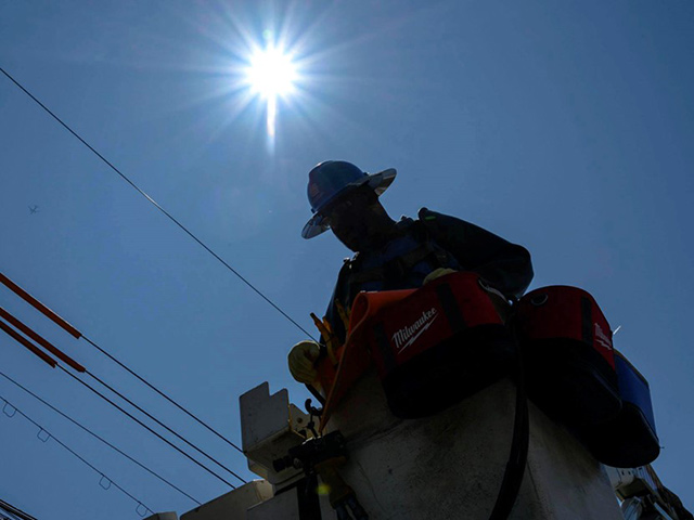 A Con Edison employee works on overhead lines while in a bucket truck lift on a sunny day.