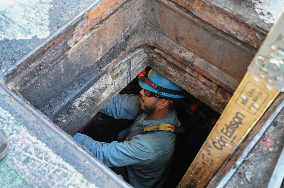 A Con Edison field employee working in a manhole during the day.