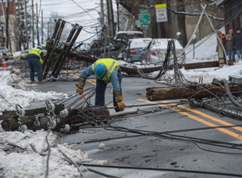 Con Edison utility workers cutting wires of multiple downed telephone poles lying across the street.