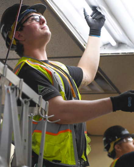 A man wearing a safety vest installing a lightbulb.