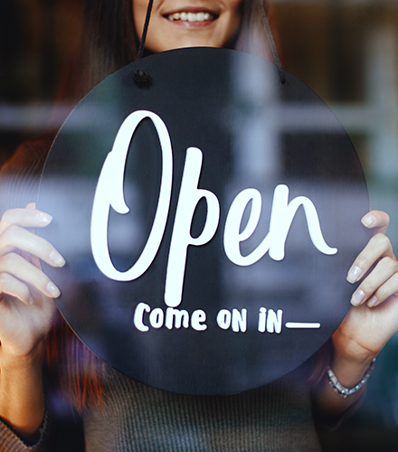 A woman standing in a shop window holding an "open" sign.
