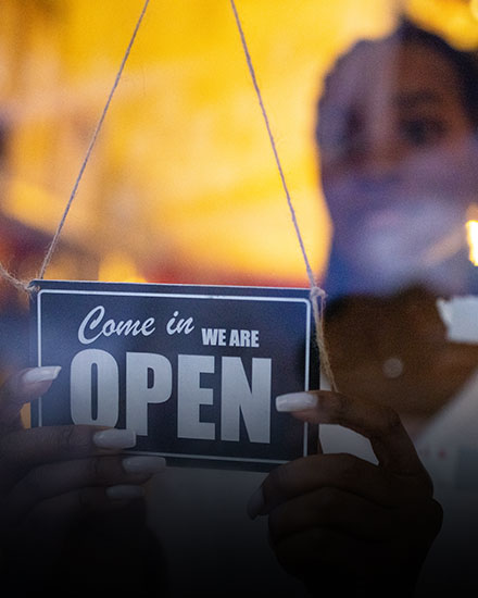 Woman putting up sign that reads "come in, we're open"