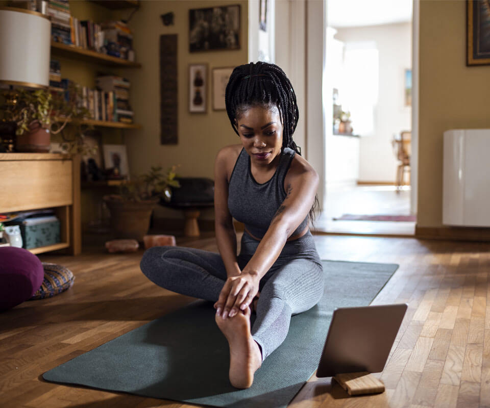 A woman is sitting on a yoga matt and stretching.