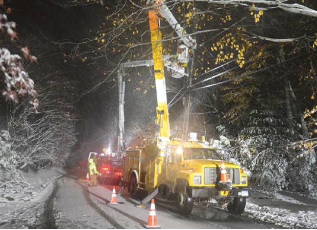 Two bucket trucks parked on a snowy road lift crews to repair overhead wires.